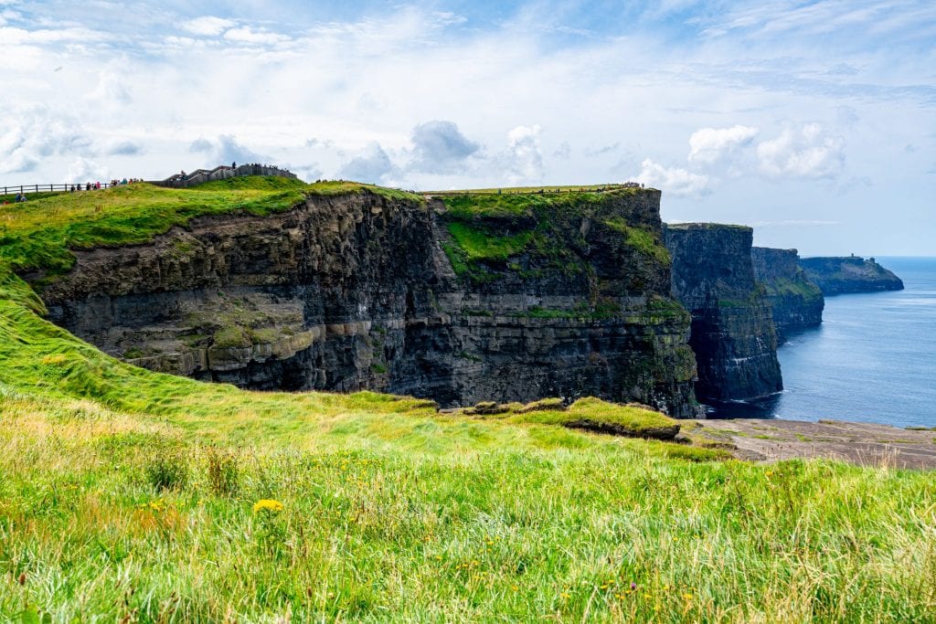 Cliffs of Moher in Ireland visible beyond a patch of bright green grass