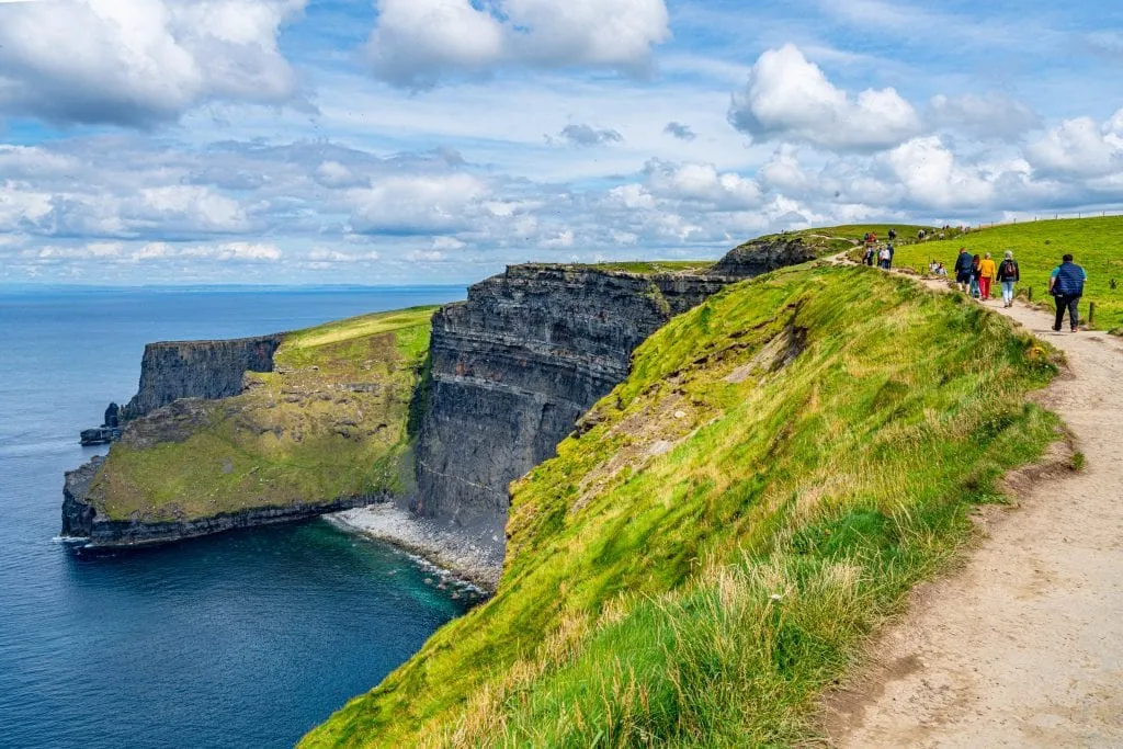  folk vandrer langs klipperne i Moher Kystvandring nær Doolin Irland, en lille strand er synlig til venstre