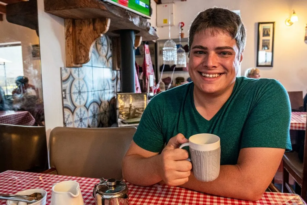 Jeremy Storm holding a cup of tea in a small cafe on Inisheer Ireland. There's a stone fireplace behind him.
