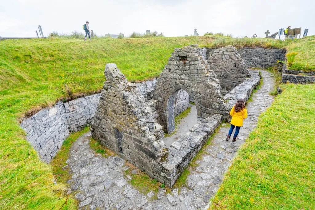 Kate Storm in a yellow raincoat walking along the edge of the sunken church on Inisheer Ireland