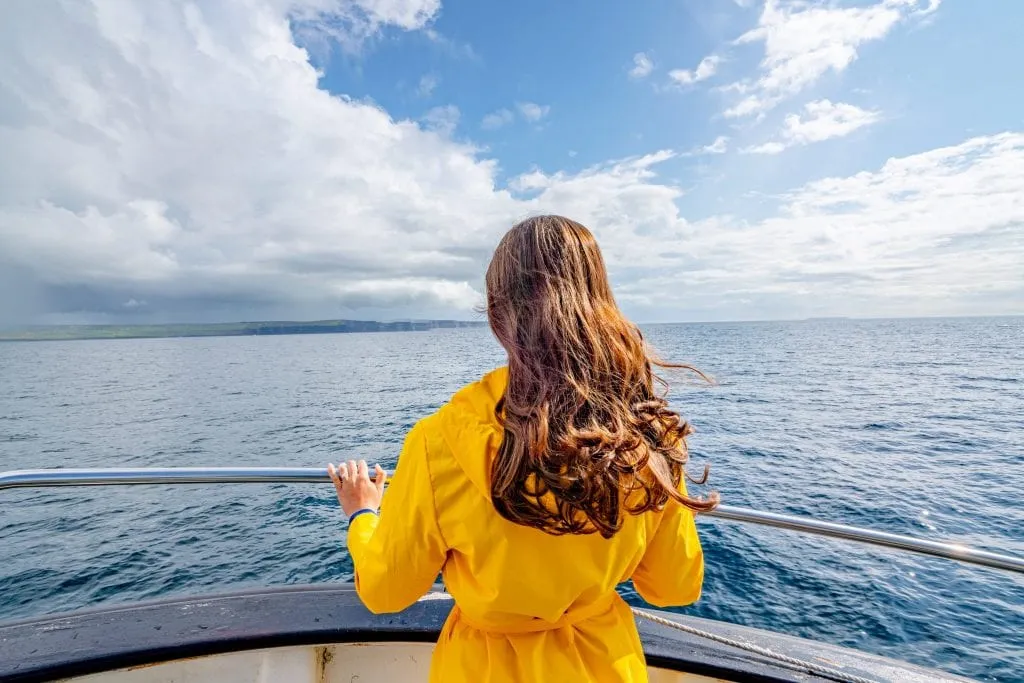 Kate Storm in a yellow raincoat on the ferry from Inisheer to Doolin. You can see the Cliffs of Moher far off in the distance.