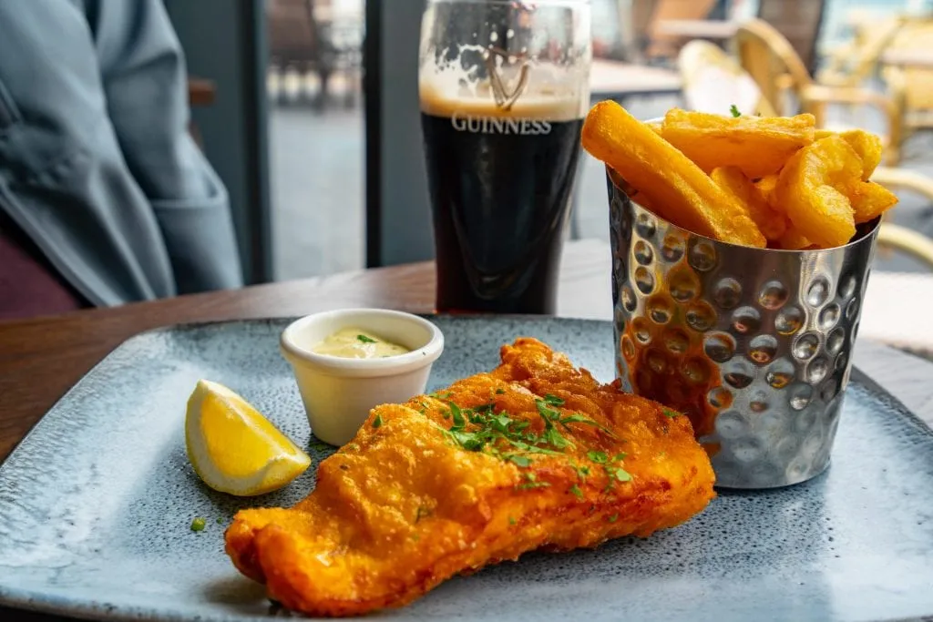 Plate of fish and chips in Ireland with a glass of Guinness in the background--a traditional Irish food meal