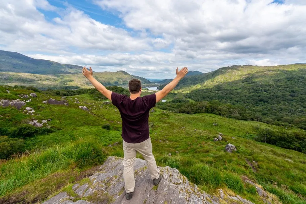 Jeremy Storm standing at an overlook in Killarney National Park, facing away from the camera with his arms in the air.