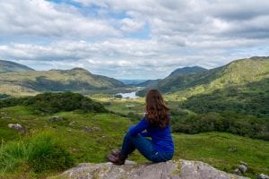 Kate Storm in a blue long-sleeved shirt overlooking Killarney Natoinal Park--a must-see spot when planning a trip to Ireland!