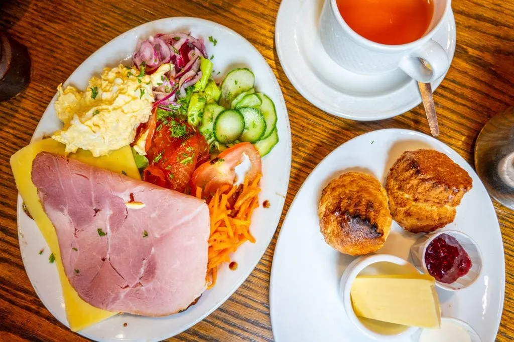 Open-faced ham sandwich shot from above with a plate of scones and cup of tea next to it