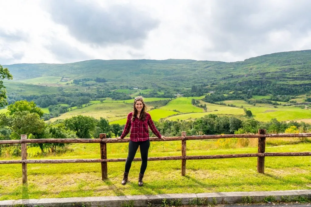 Kate Storm standing against a split level fence with Irish countyside in the background--plenty of this to be found on an Ireland road trip!