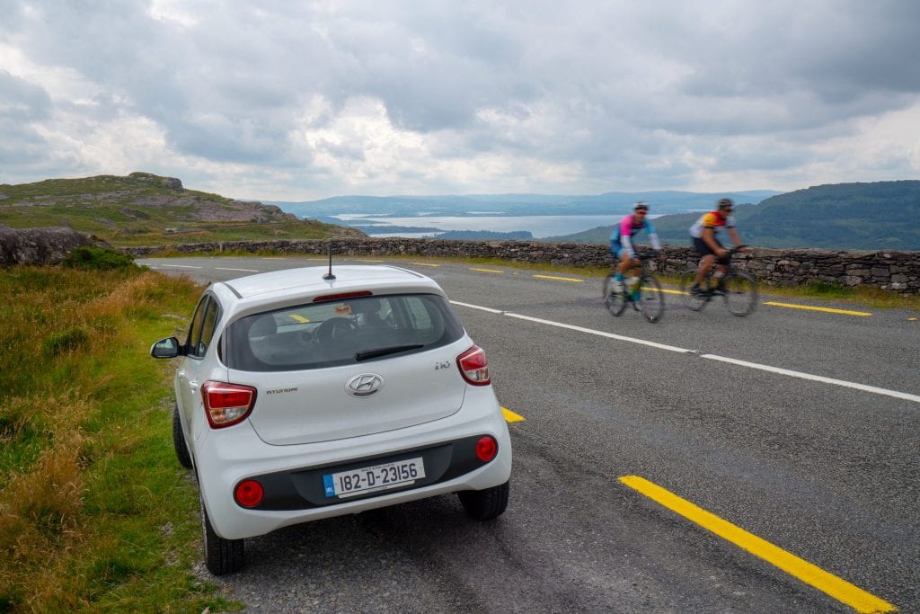 Photo of car parked on the side of the road during an Ireland road trip. Two bikers are visible passing by on the right side of the photo.