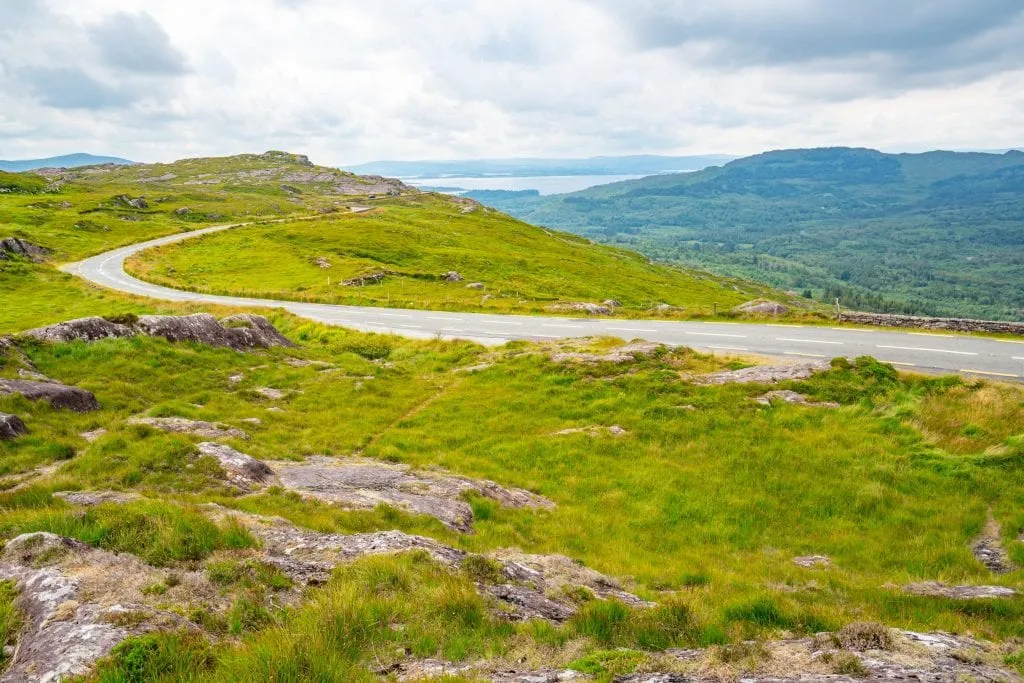 Empty curving road in Ireland with green fields on either side--it's worth making sure you have all the necessary road trip essentials before starting an epic drive out here!