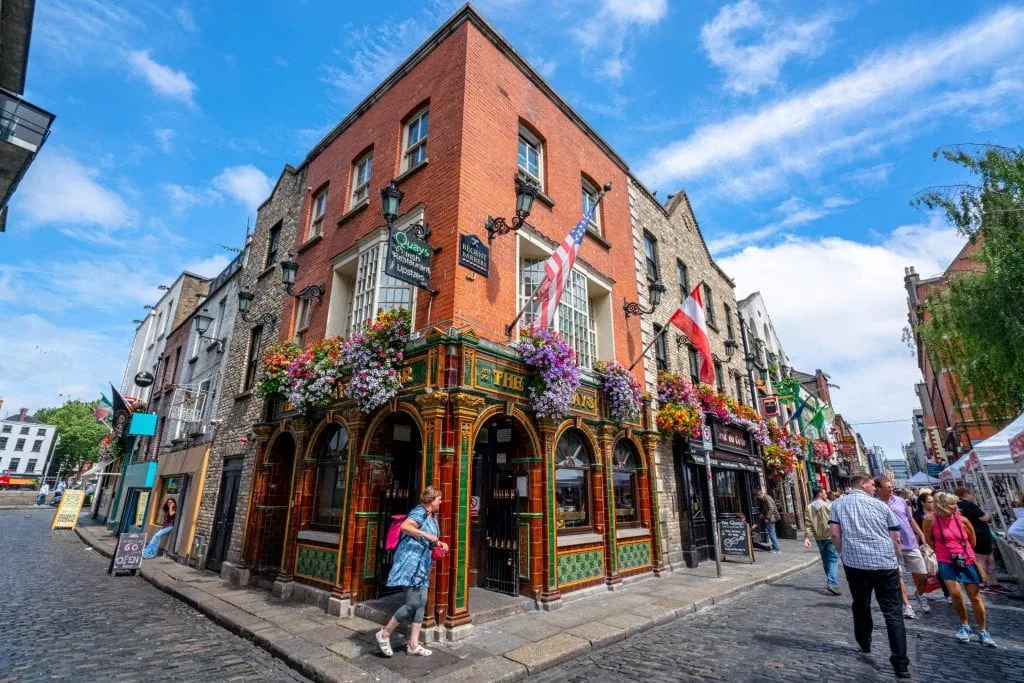 Photo of building in Dublin Ireland with flowers and flags on it. There are people walking in front of the building.