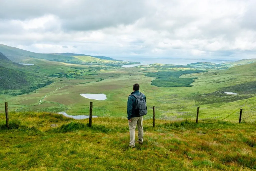 Jeremy Storm carrying a pacsafe backpack and wearing a gray jacket, looking out over Conor Pass in Ireland