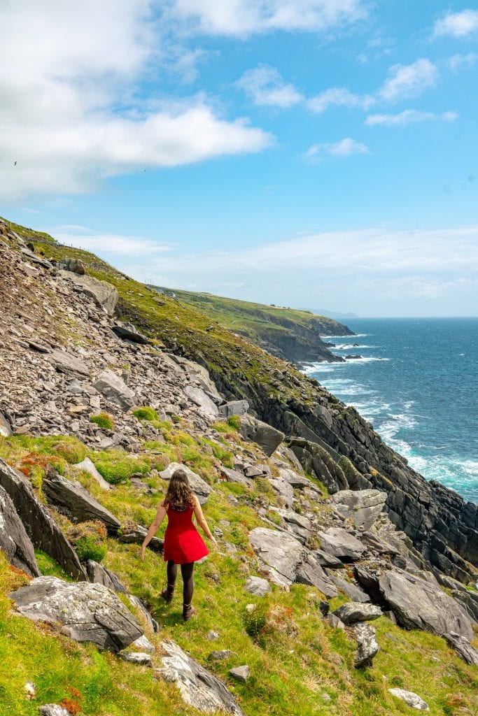 Kate Storm in a red dress walking along a cliff on Slea Head Drive Ireland