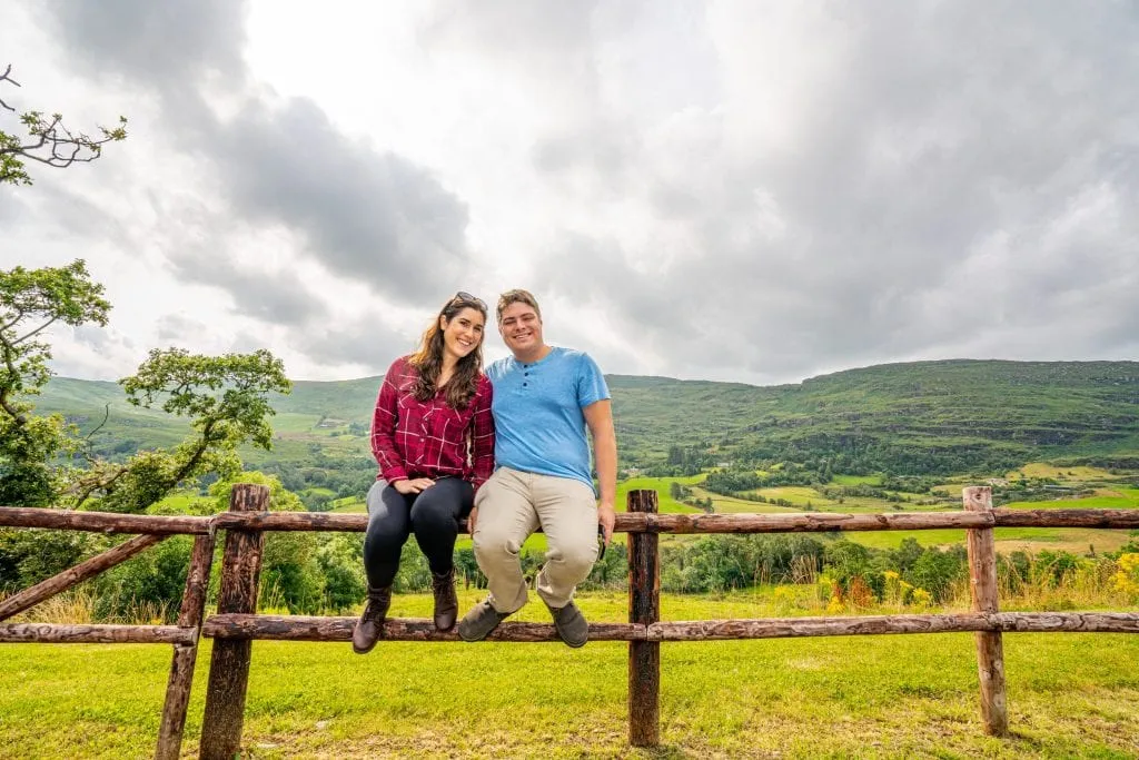 Kate Storm and Jeremy Storm sitting on a split-level fence in Ireland while on an Ireland road trip