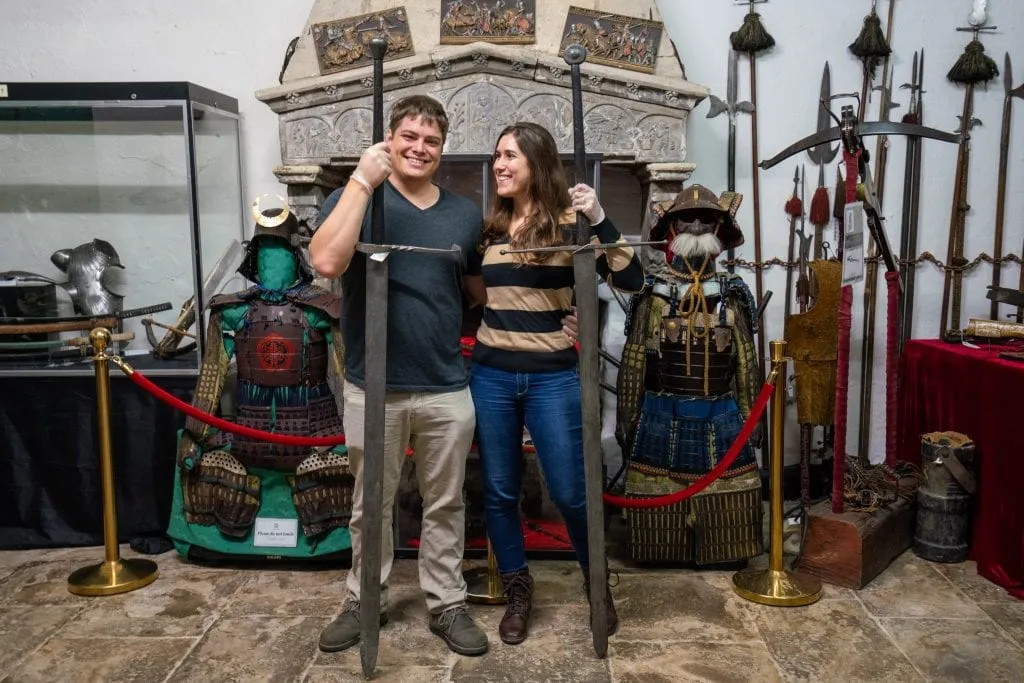 Kate Storm and Jeremy Storm hold tall swords in front of other antique weapons at Belleek Castle in Ireland