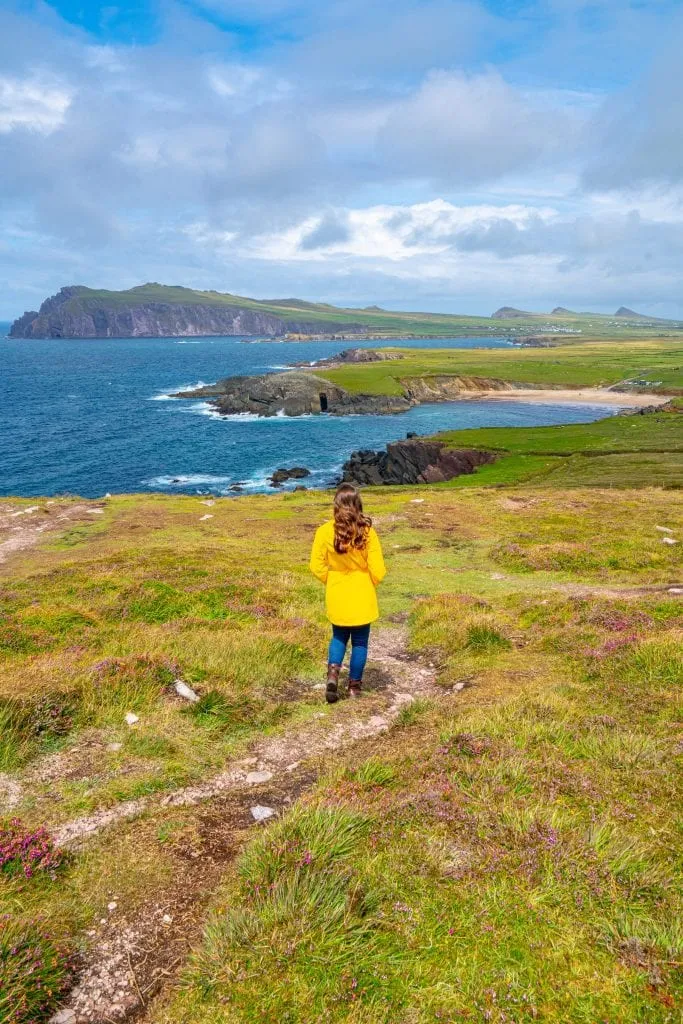 Kate Storm in a yellow raincoat at Dunmore Head Ireland, with the Three Sisters visible in the background