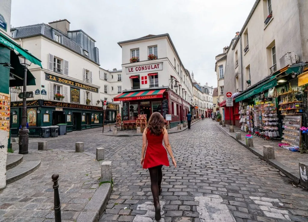 Kate Storm in a red dress in front of La Consulat cafe in Montmartre, one of the most instagrammable places in Paris