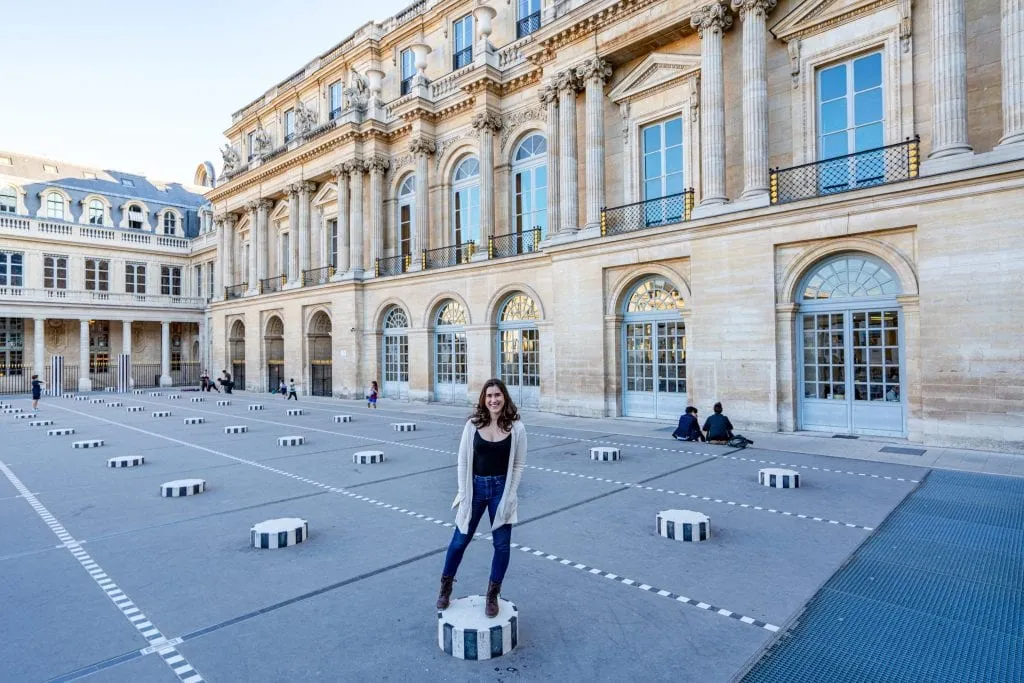 Kate Storm in a black shirt and cream cardigan standing on one of the Colonnes de Buren in Paris France--if you like quirky photo ops, definitely come here as part of your weekend trip to Paris!