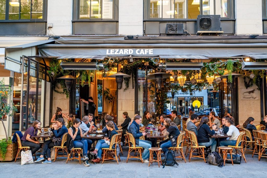 Busy cafe in Paris with diners in front of it--experiences like this are an idyllic part of any trip to Paris, cost aside.