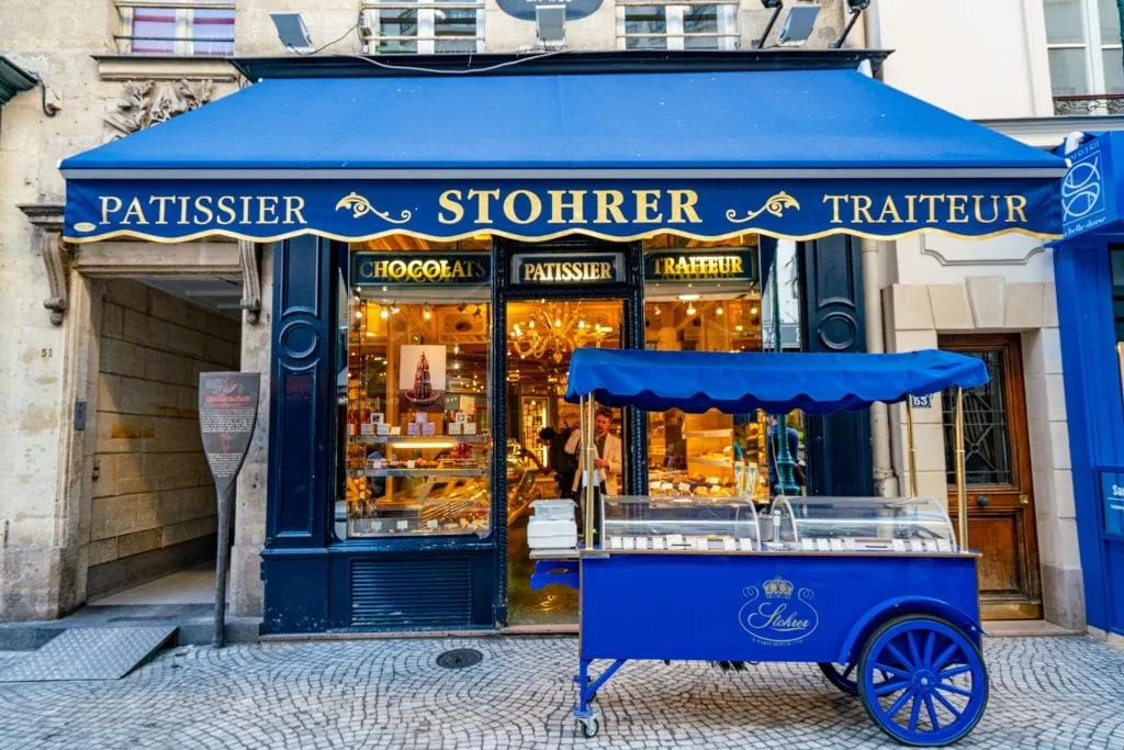 Facade of Patisserie Stohrer in Paris with a blue awning and blue cart out front--definitely stop by here when exploring Paris off the beaten path.