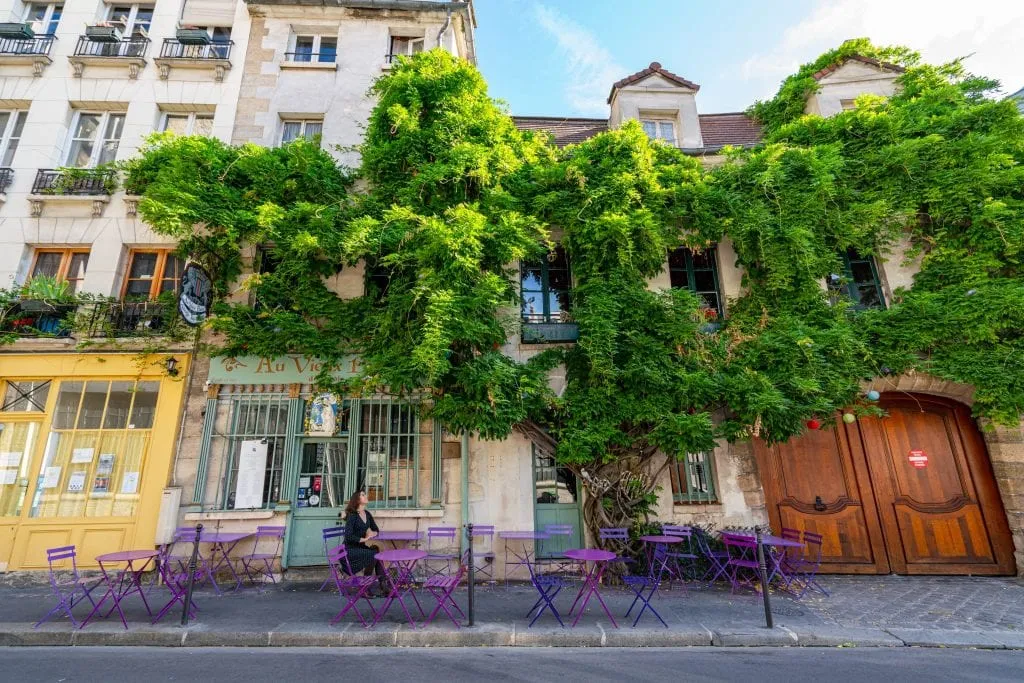 Kate Storm in a gray dress sitting in front of Cafe Au Vieux, one of the most instagrammable spots in Paris