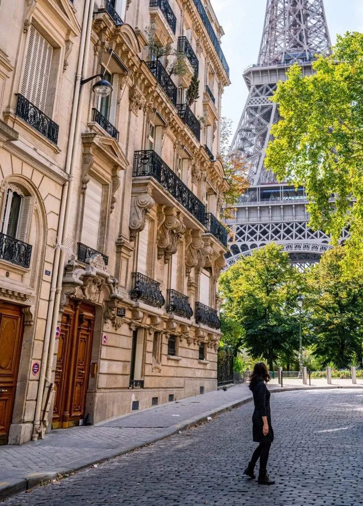 Kate Storm in a gray dress standing in Rue de l'Universite in Paris with the Eiffel Tower behind her