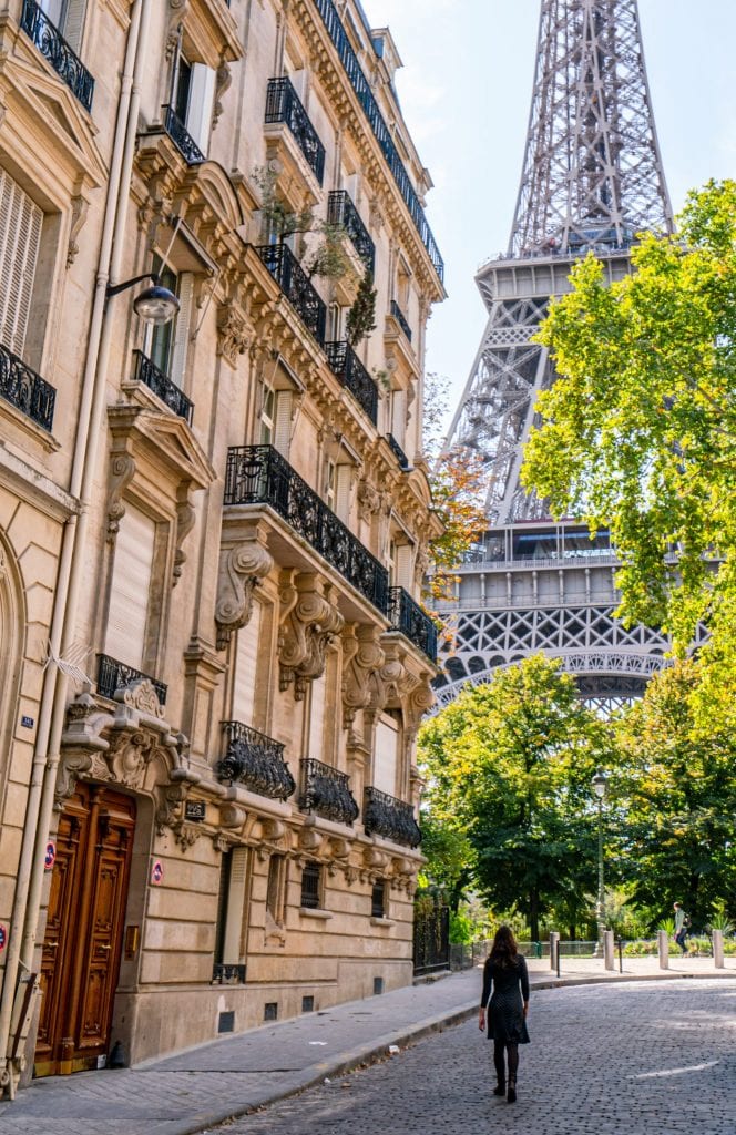 Kate Storm in a gray dress standing in Rue de l'Universite in Paris with the Eiffel Tower behind her