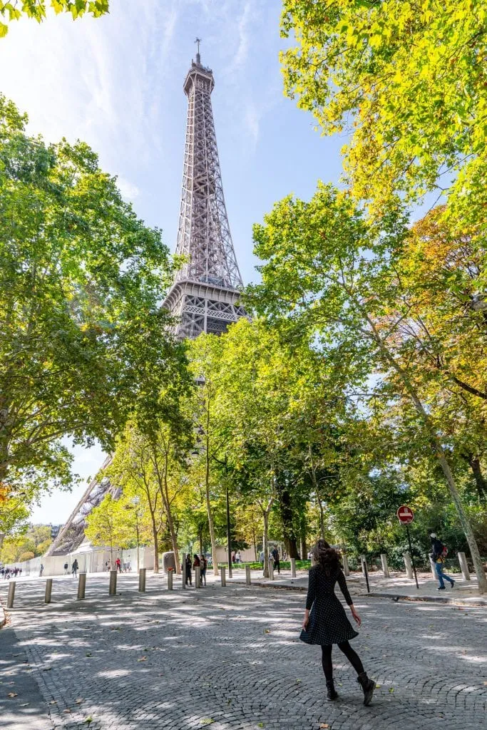 Kate Storm standing in an empty road in front of the Eiffel Tower with trees framing the view