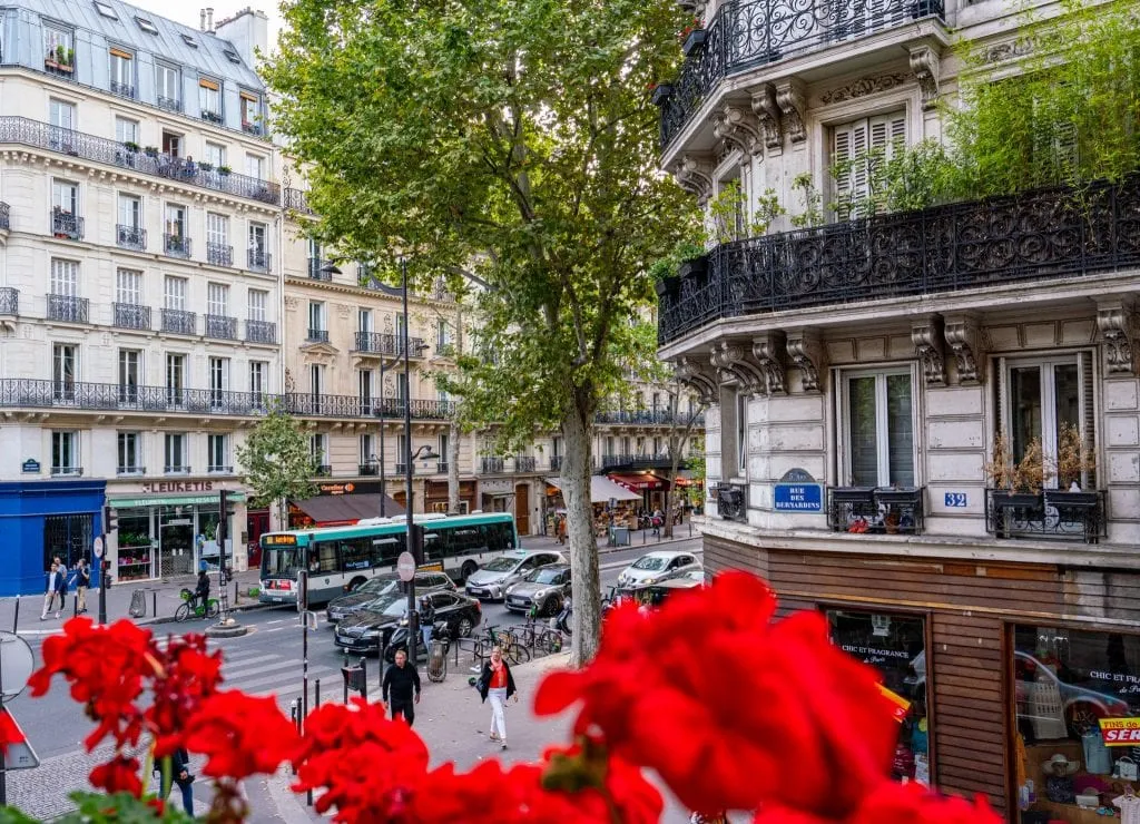 Photo of a Parisian Street looking out a window at Hotel Abbatial Saint Germain with red flowers in the foreground--this is a great pick if you're looking for somewhere to spend your weekend in Paris!