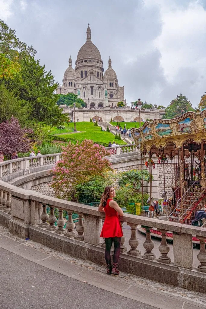 Kate Storm trong chiếc váy đỏ đứng với vòng quay ngựa gỗ và nhà thờ Sacre Coeur ở phía sau - đây là một trong những địa điểm có tính Instagram nhất ở Paris!