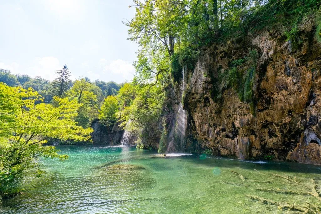 Small waterfall pouring into a shallow lake as seen when visiting Plitvice Lakes National Park Croatia