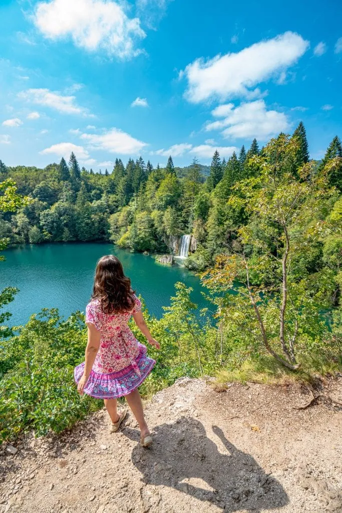 kate storm in a pink dress overlooking a waterfall in plitivice lakes national park, one of the best places to visit on an itinerary croatia 10 days