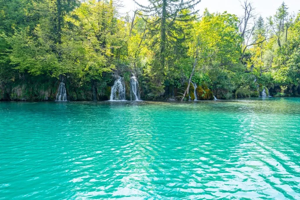 bright turquoise lake with small waterfalls visible in the distance, as seen when visiting Plitvice Lakes Croatia