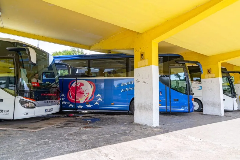 A group of white and blue buses parked under a yellow awning at the bus station in Trogir--riding a bus is almost certainly going to be part of your 10 day Croatia itinerary!