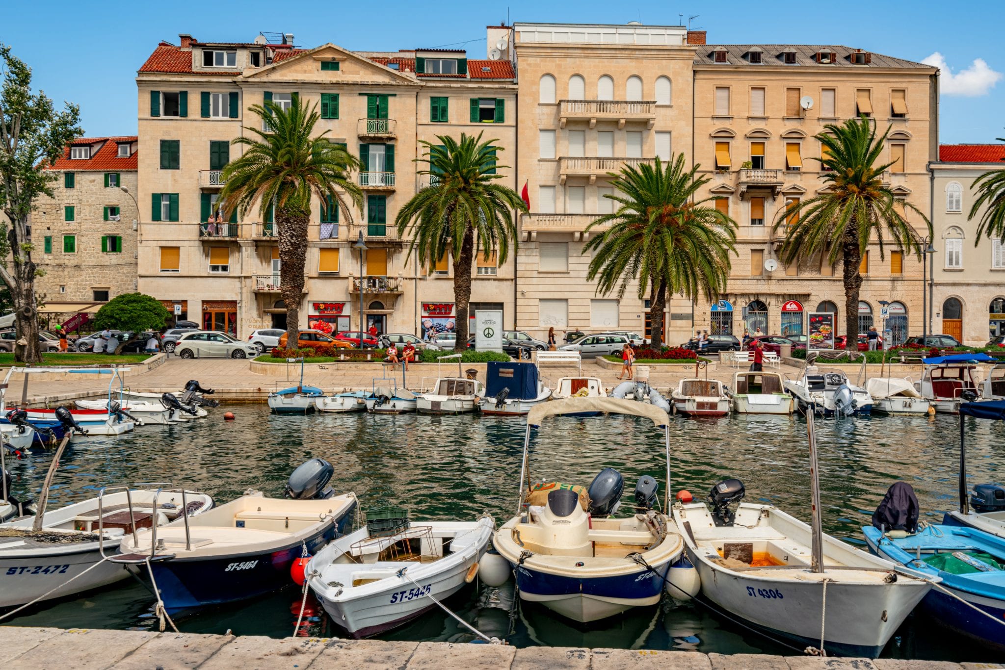 View of Split Croatia Harbor with small boats in the foreground and palm trees in front of buildings in the background