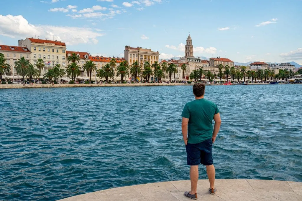  Jeremy Storm in una camicia turchese in piedi sul bordo dell'acqua, guardando lontano dalla telecamera e verso Spalato in lontananza--sia che si visita Spalato o Dubrovnik, viste sull'Adriatico abbondano!