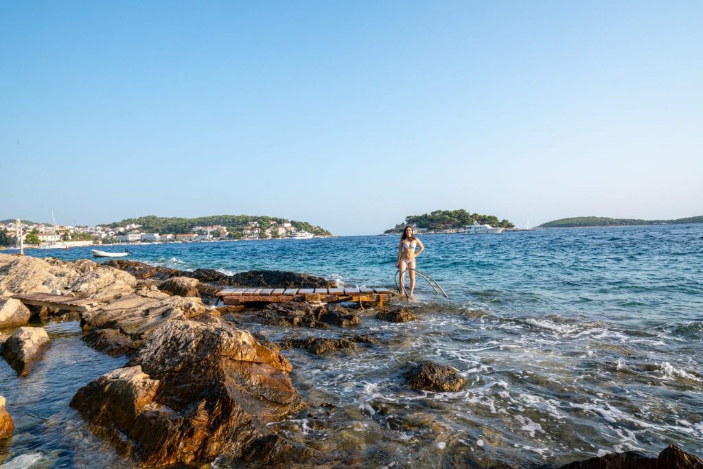 Kate Storm standing on the rocky coastline of Hvar--swimming off the rocks is one of the best things to do in Hvar!