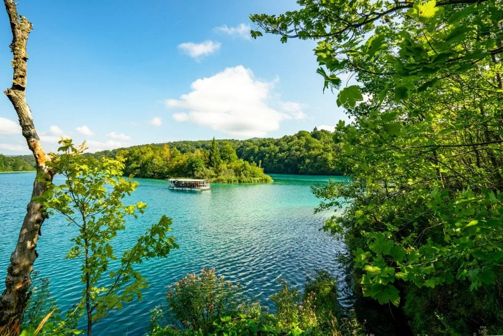 Ferry crossing Lake Kozjak in Plitvice Lakes National Park in Croatia as seen from above through a patch of trees