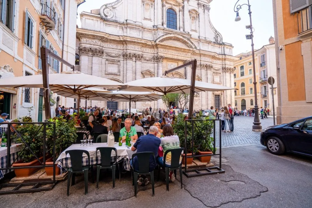 Piazza in Rome with church visible in the background and a restaurant with people dining outside in the foreground. These Rome travel tips will help you find pretty corners like this!