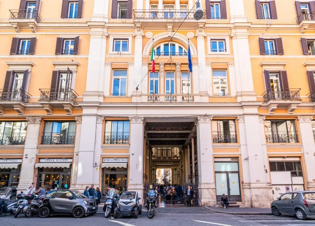 Entrance to the Galleria Sciarra in Rome, showing a yellow building exterior with vespas parked out front