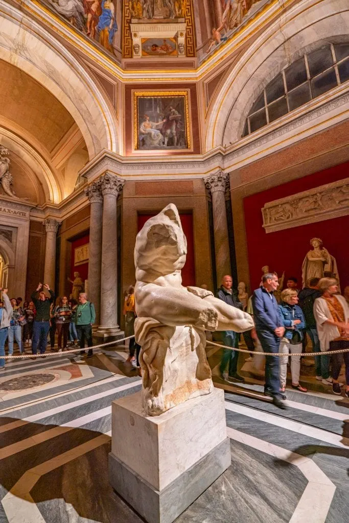 Statue that inspired The Thinker displayed in the Vatican, with tourists visible in the background.