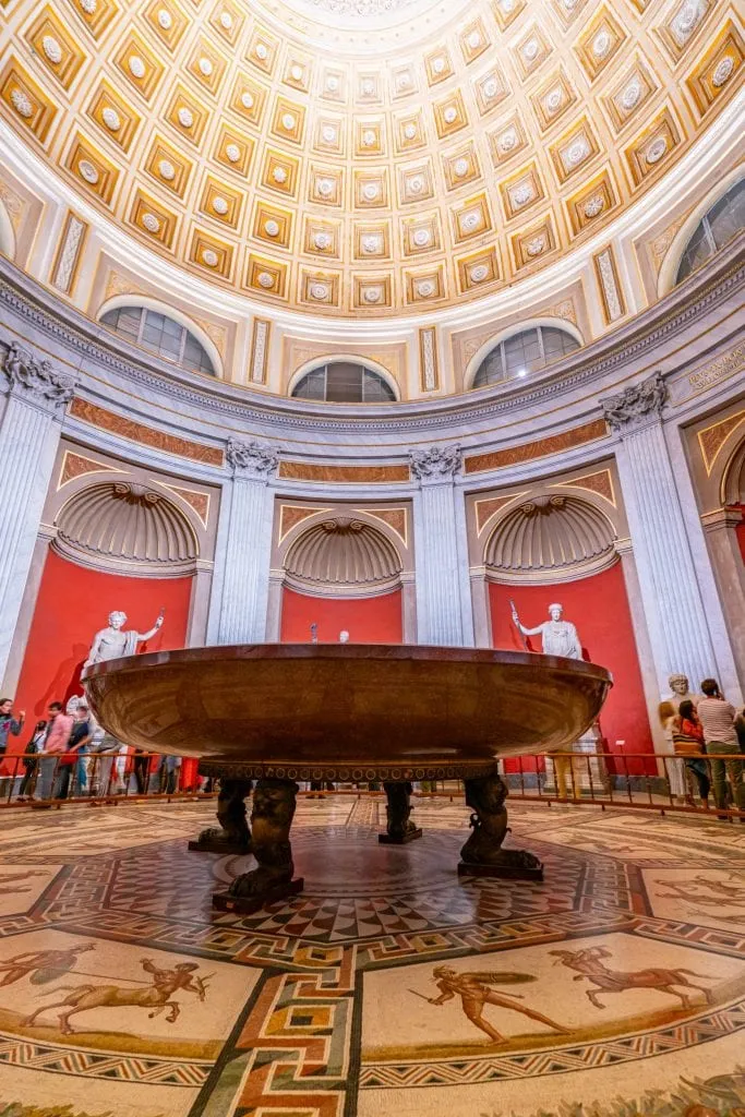 Large basin as seen when visiting the Vatican Museums, housed underneath a dome. Walls in the background are painted red.