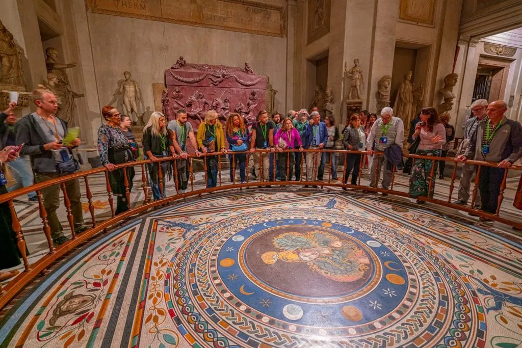A beautiful mosaic floor in the Vatican Museums, with tourists standing around the edge of it snapping photos