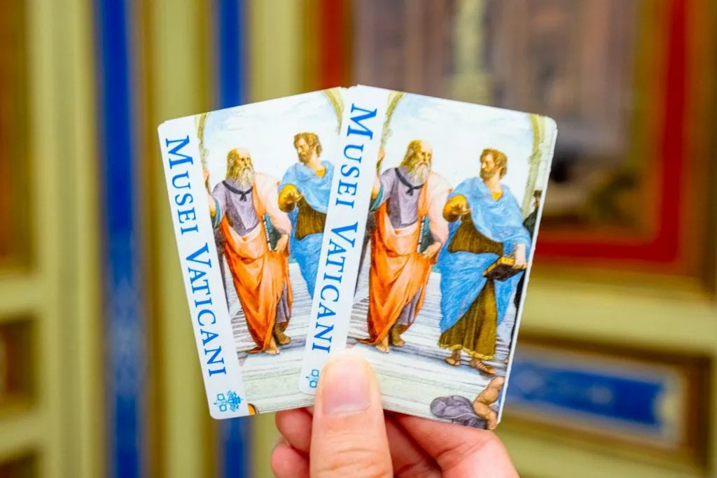 Two tickets for the Vatican Museums being held up in front of a colorful wall--pre-booking these tickets is one of the most important Vatican travel tips