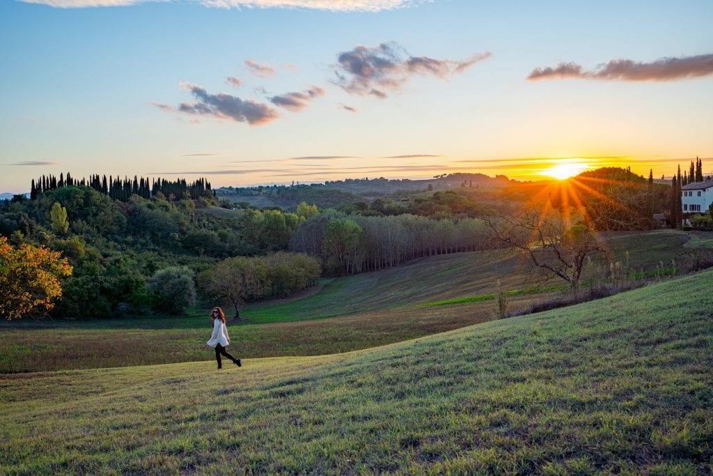 Kate Storm in the Tuscan countryside at sunset with a sun flare on the right side of the photo--Tuscan sunsets are an epic part of any Tuscany road trip itinerary.