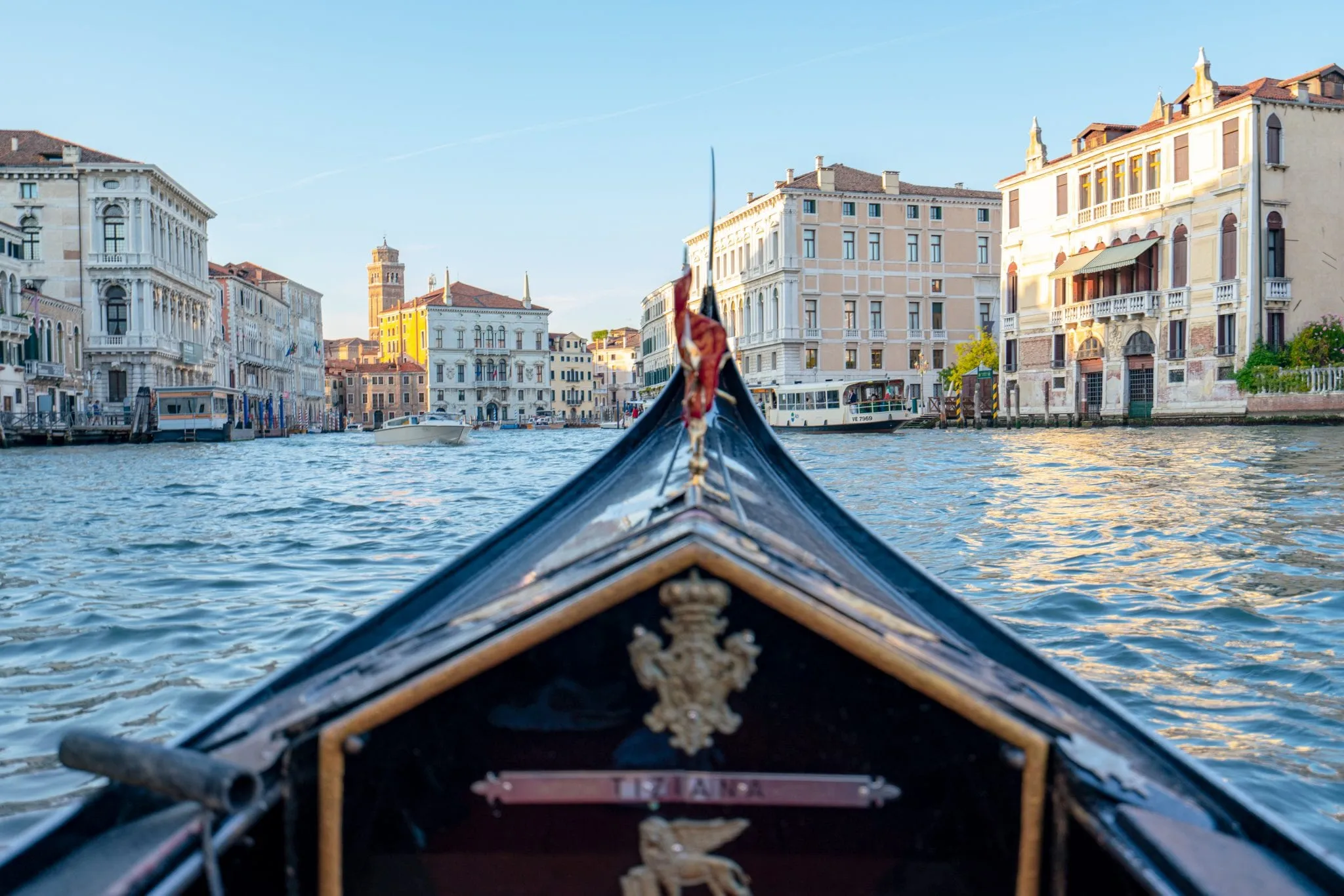 A photo of the front of a Venetian gondola in the foreground with the Grand Canal in the background--the absolute best views of Venice can be found from inside a gondola!