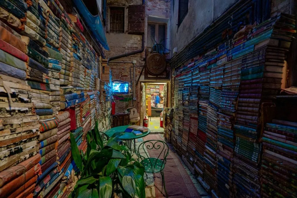 Entrance to Libreria Acqua Alta at night, with books stacked on either side of the walkway