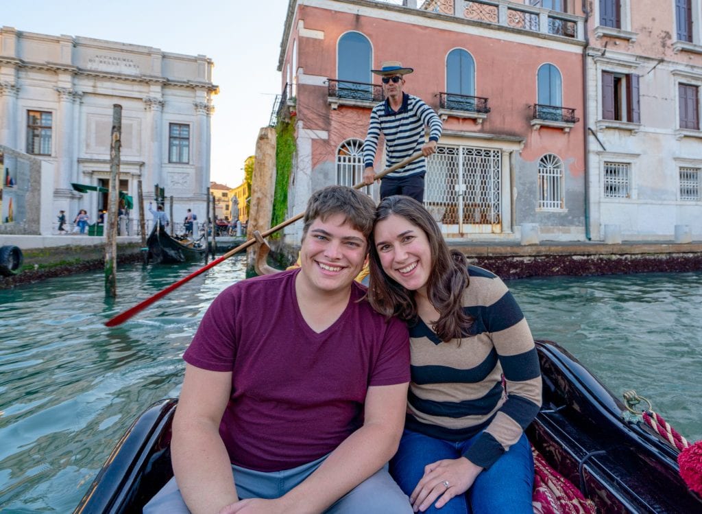 Couple sitting in a gondola in Venice with a gondolier visible behind them