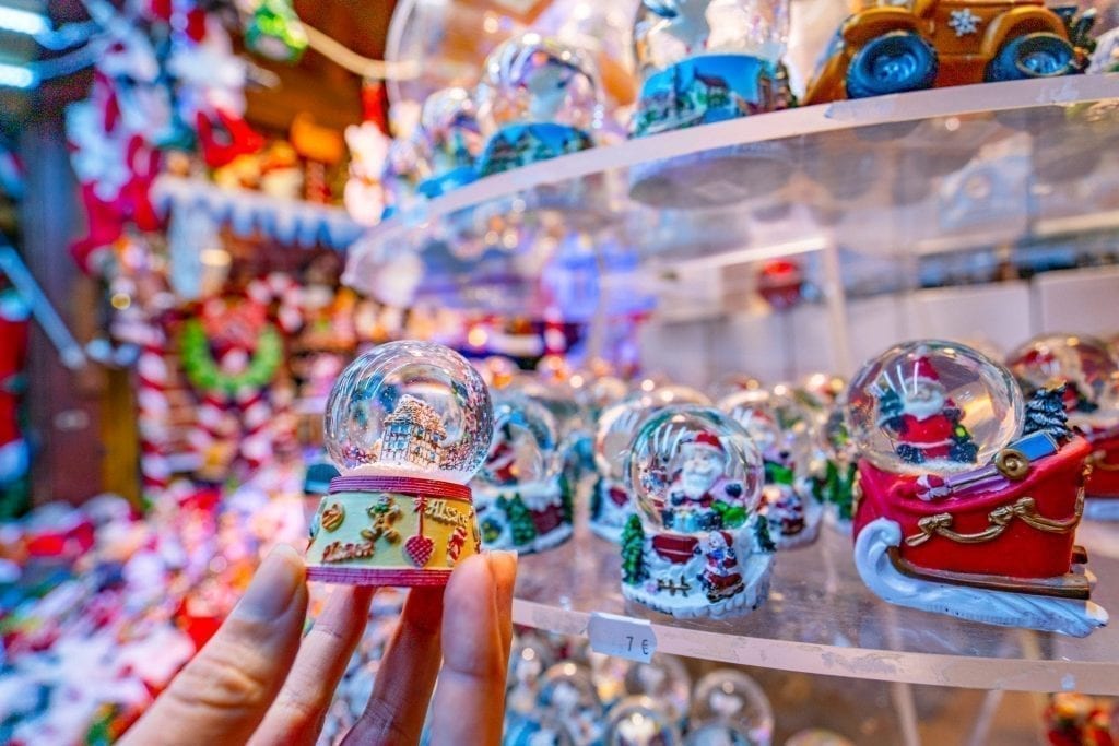 Small snow globe being held up while shopping at Colmar Christmas markets