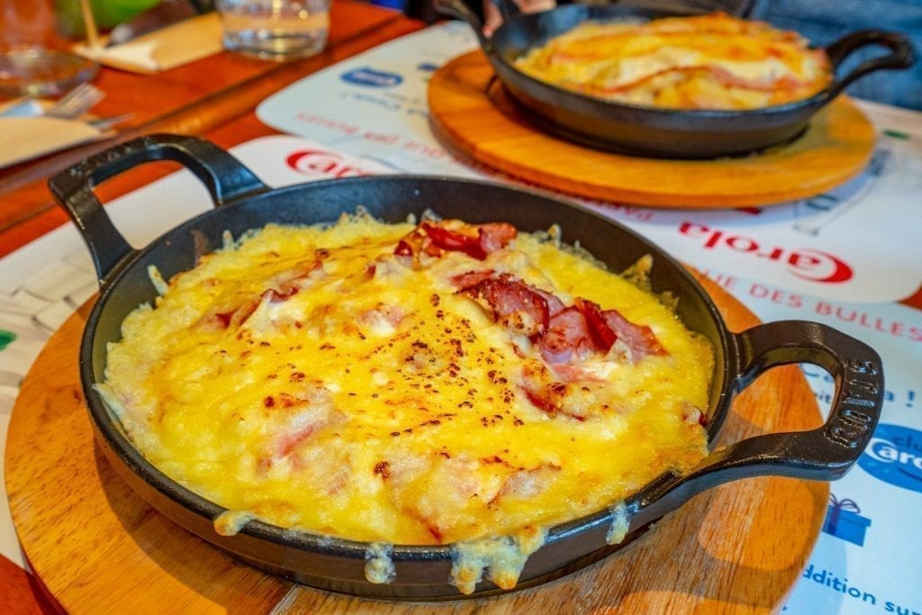 Cheesy rosti served in a round cast iron pan--this is a typical food in Alsace and deserves to be on your list of things to do in Strasbourg France!