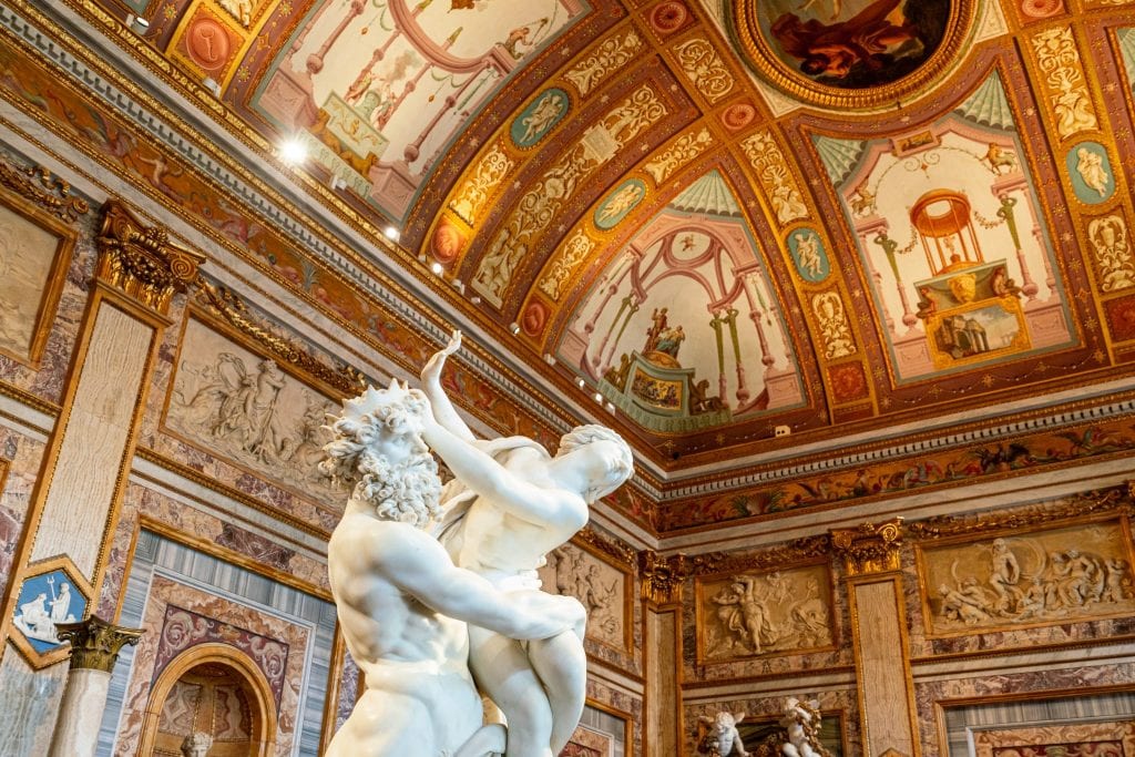 Interior of the Galleria Borghese taken while looking up at gilded ceiling witha white statue in the foreground--as you work through these Rome travel tips, keep in mind that you'll want to book skip the line tickets for popular places like this!