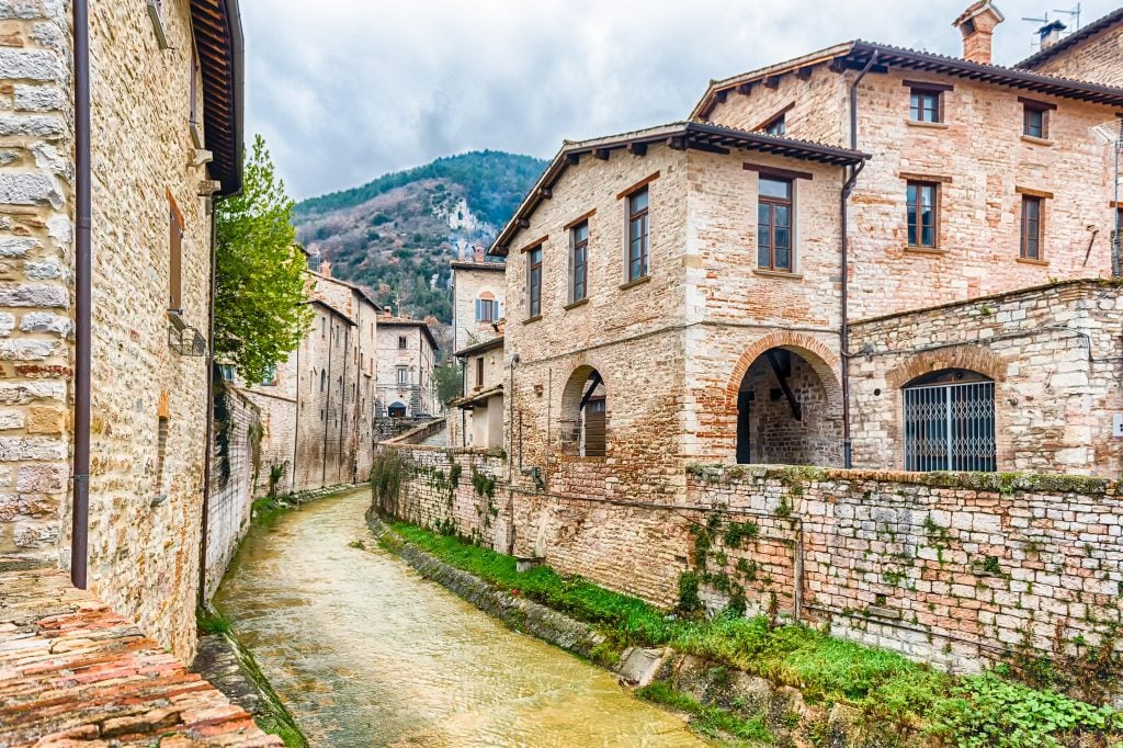 view of a river running between stone buildings in gubbio, one of the prettiest small villages in italy